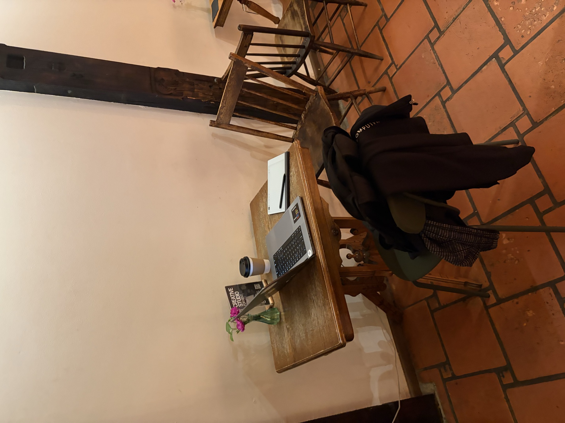 The real café corner, with a wooden table, terracotta tiles, pink flowers, a laptop, and a reMarkable tablet.